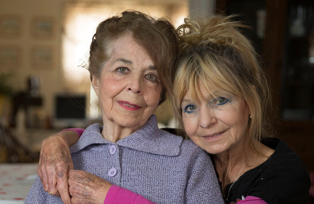 Older woman and adult daughter embracing at home, showing family support for aging loved ones and caregiving.