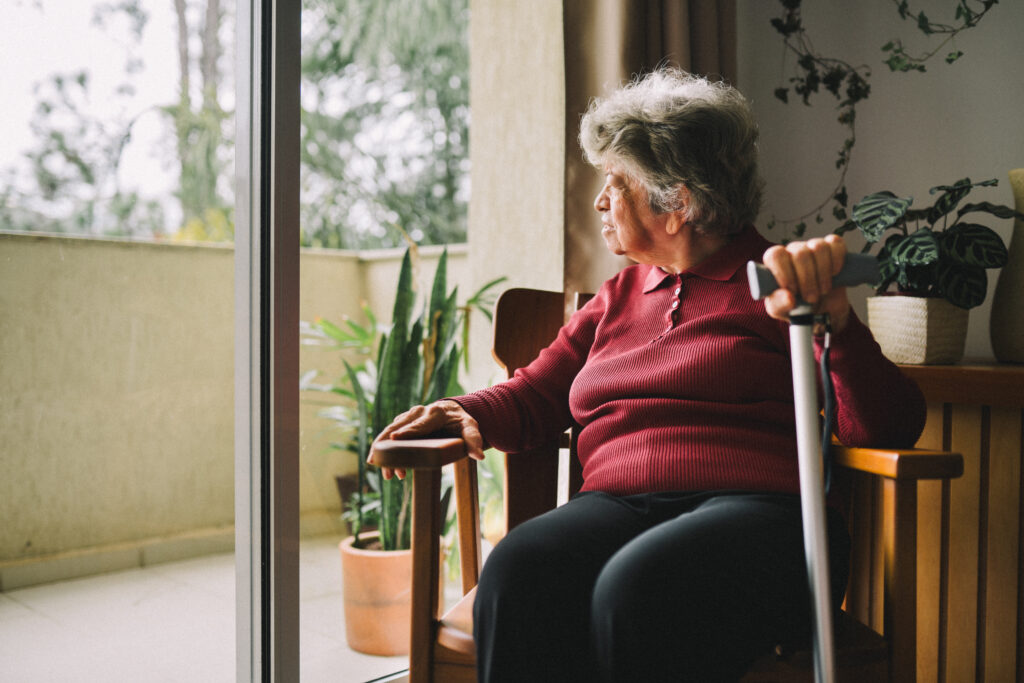 Older woman with a cane stares out her window to a patio