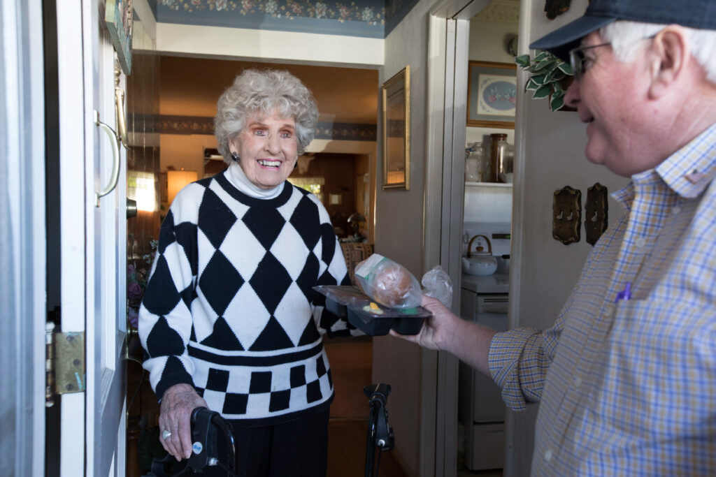 Meals on Wheels volunteer delivers a prepared meal to an older adult client at her home.