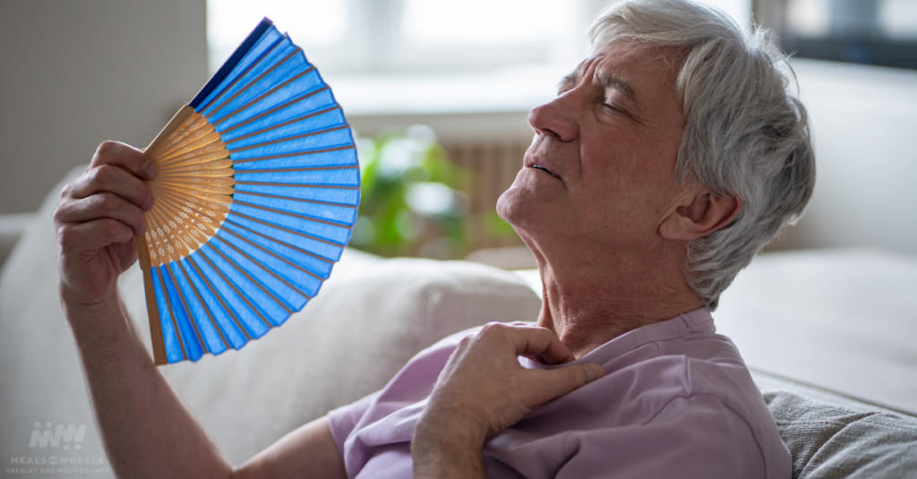 Older adult cooling off with a handheld fan during hot weather, highlighting heat safety and dehydration prevention for older adults.