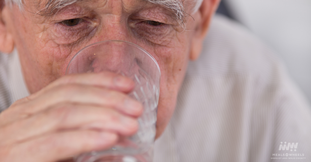 Close-up of an older adult drinking a glass of water, highlighting the importance of hydration and dehydration prevention during summer heatwaves.